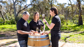 Three people tasting wine from a barrel in a bush setting in the Barossa Valley